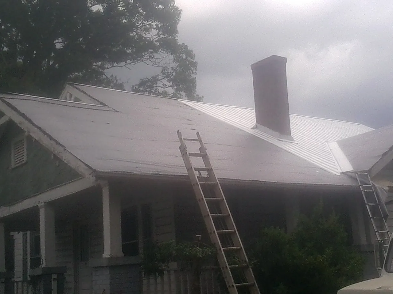 Ladders against a metal roof on an older home with a brick chimney in Derby