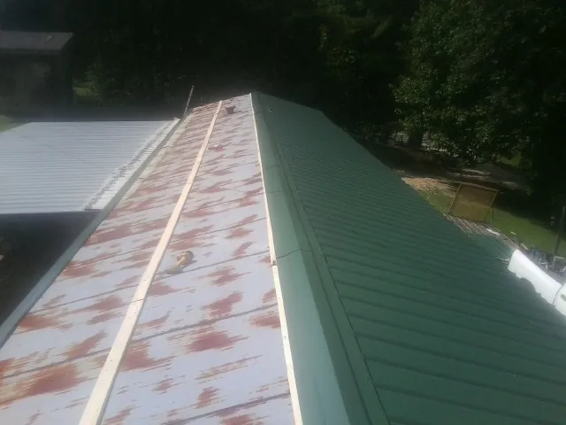 Old rusted panels beside newly installed green metal roofing — Wind Damage Roof Repair by Roofing Brothers in Derby