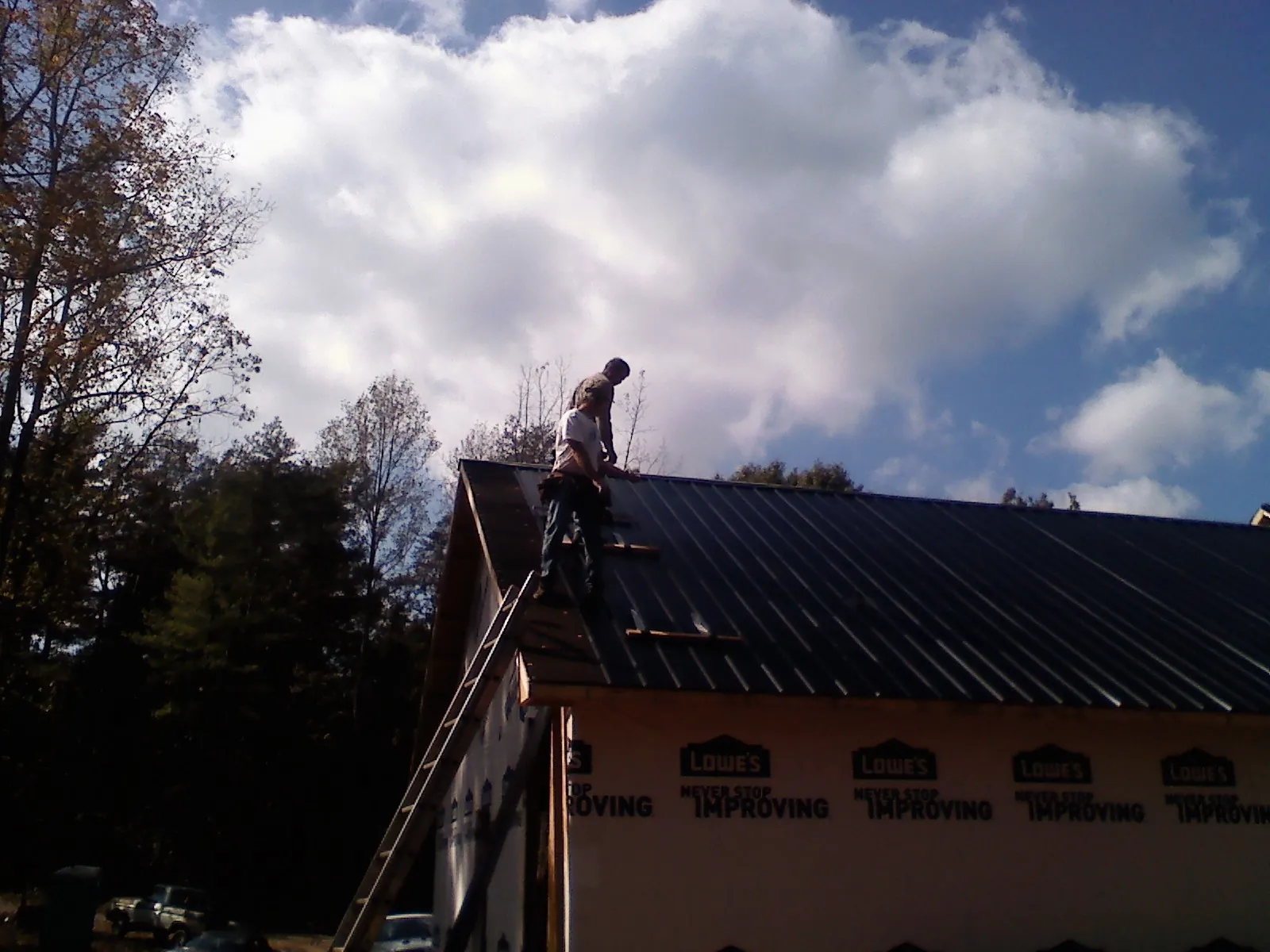 Roofer fastening dark metal panels high against a cloudy sky, from a Roof Inspection job in Derby