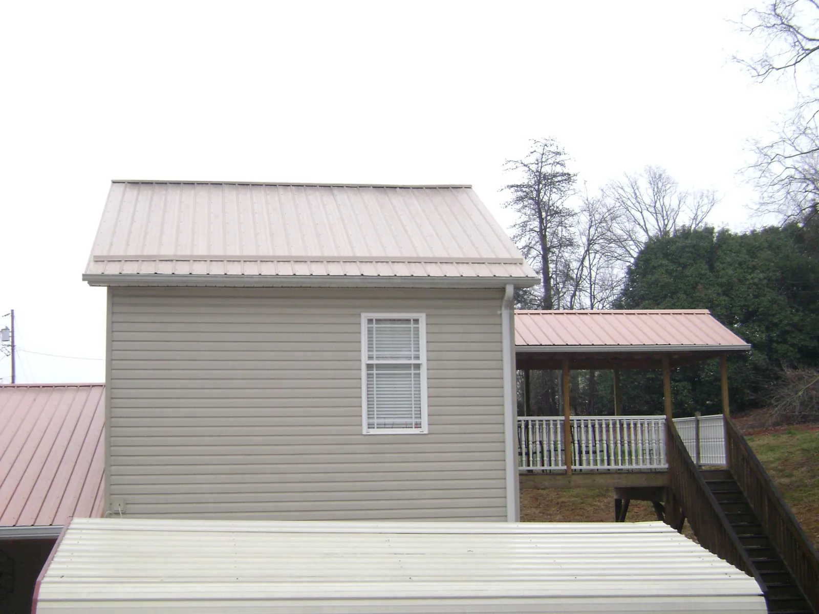 Tan metal roofs on a two story addition and attached porch, from a Roof Replacement job in Derby